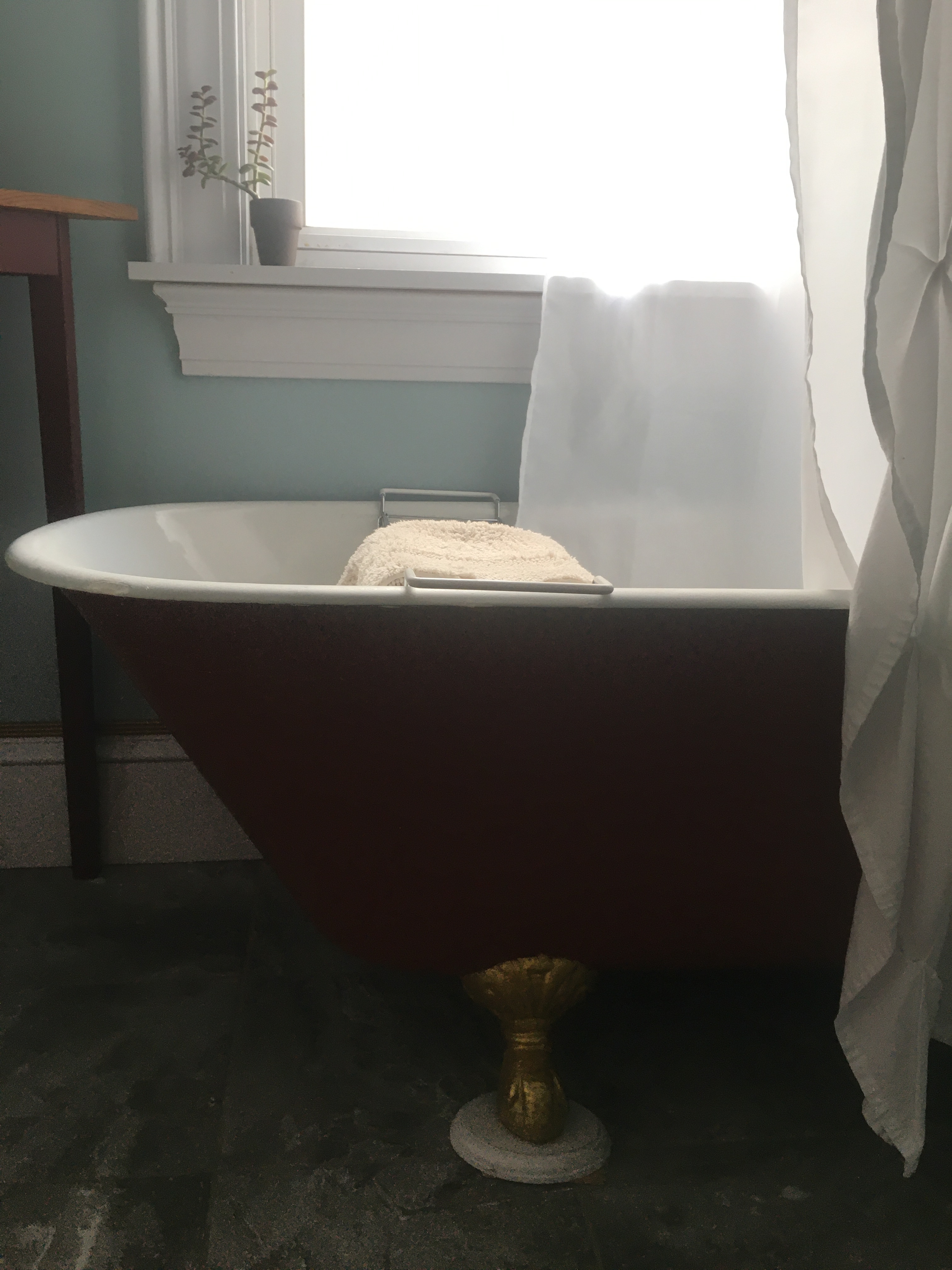 Clawfoot bathtub with red exterior and gold feet in soft light with a white shower curtain