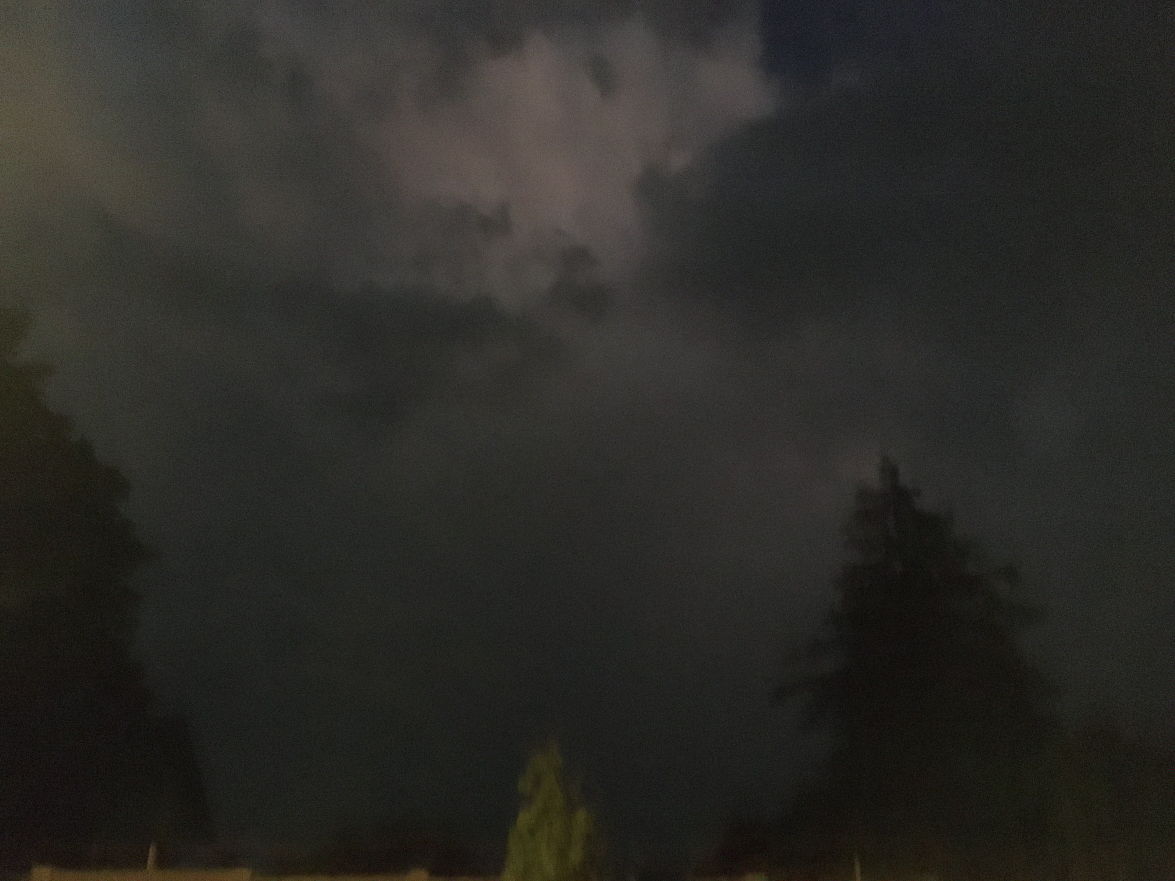 another dark sky with clouds with a few dark trees silhouetted
