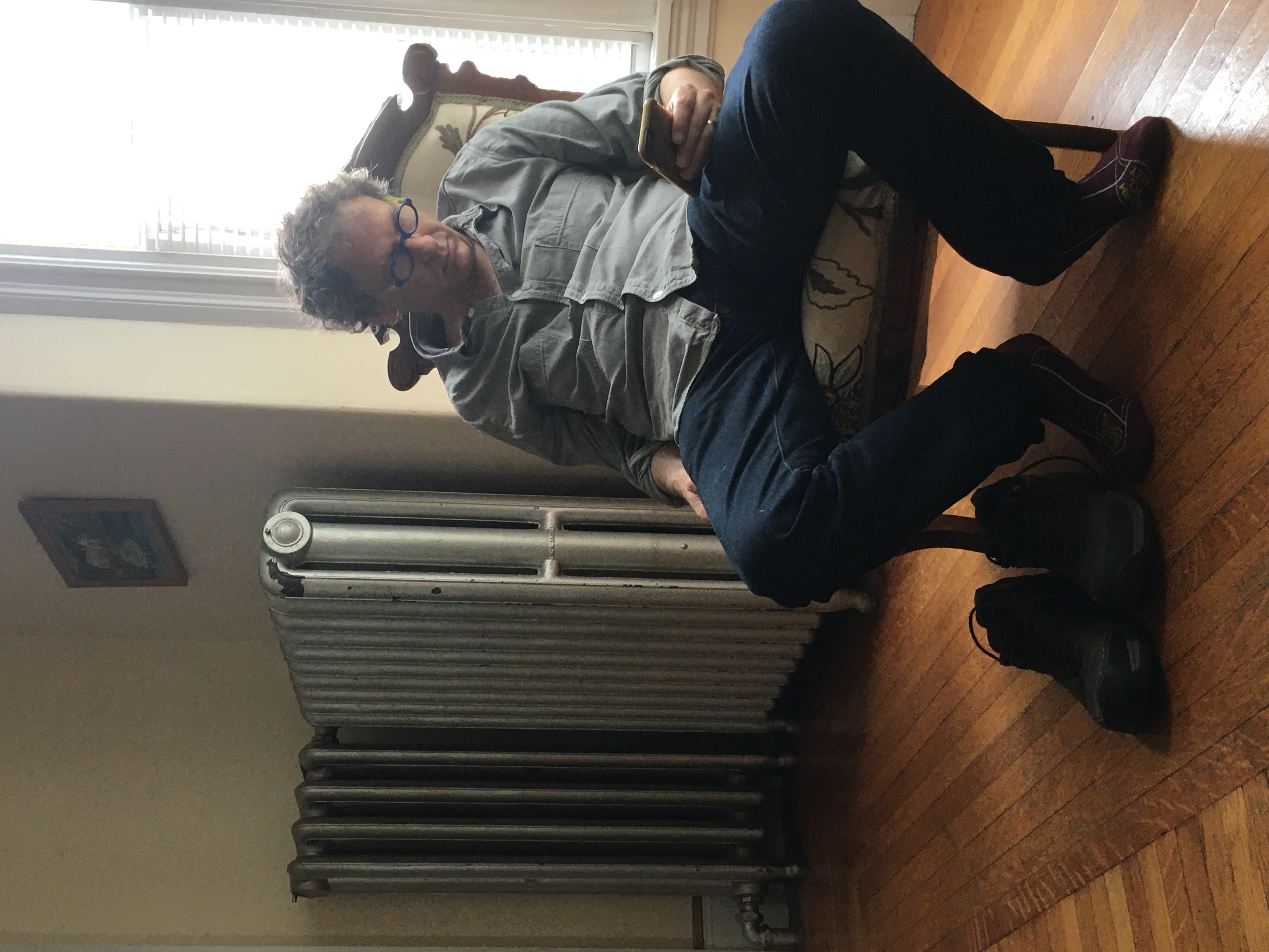 man in chair slouching and almost sleeping with radiator heater behind him.