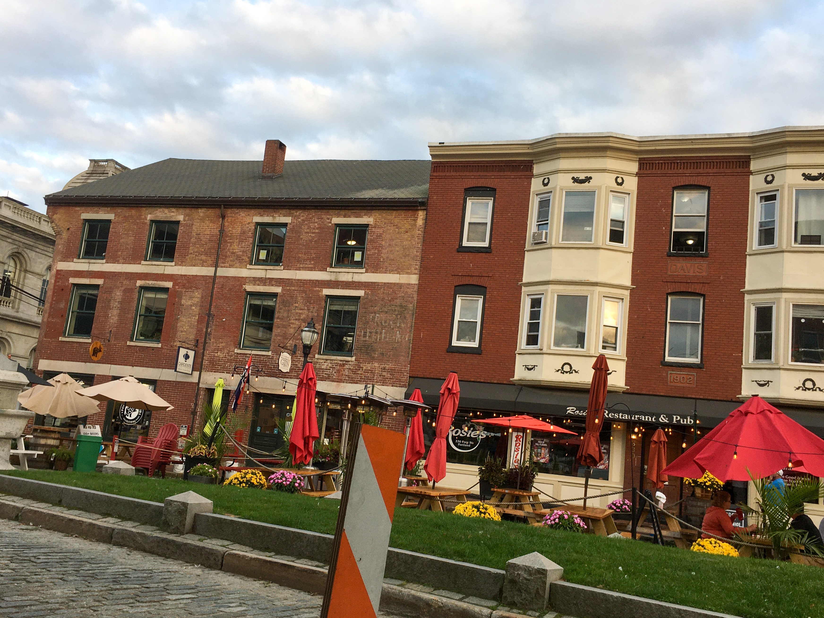 more buildings and people sitting out on a cobblestone street