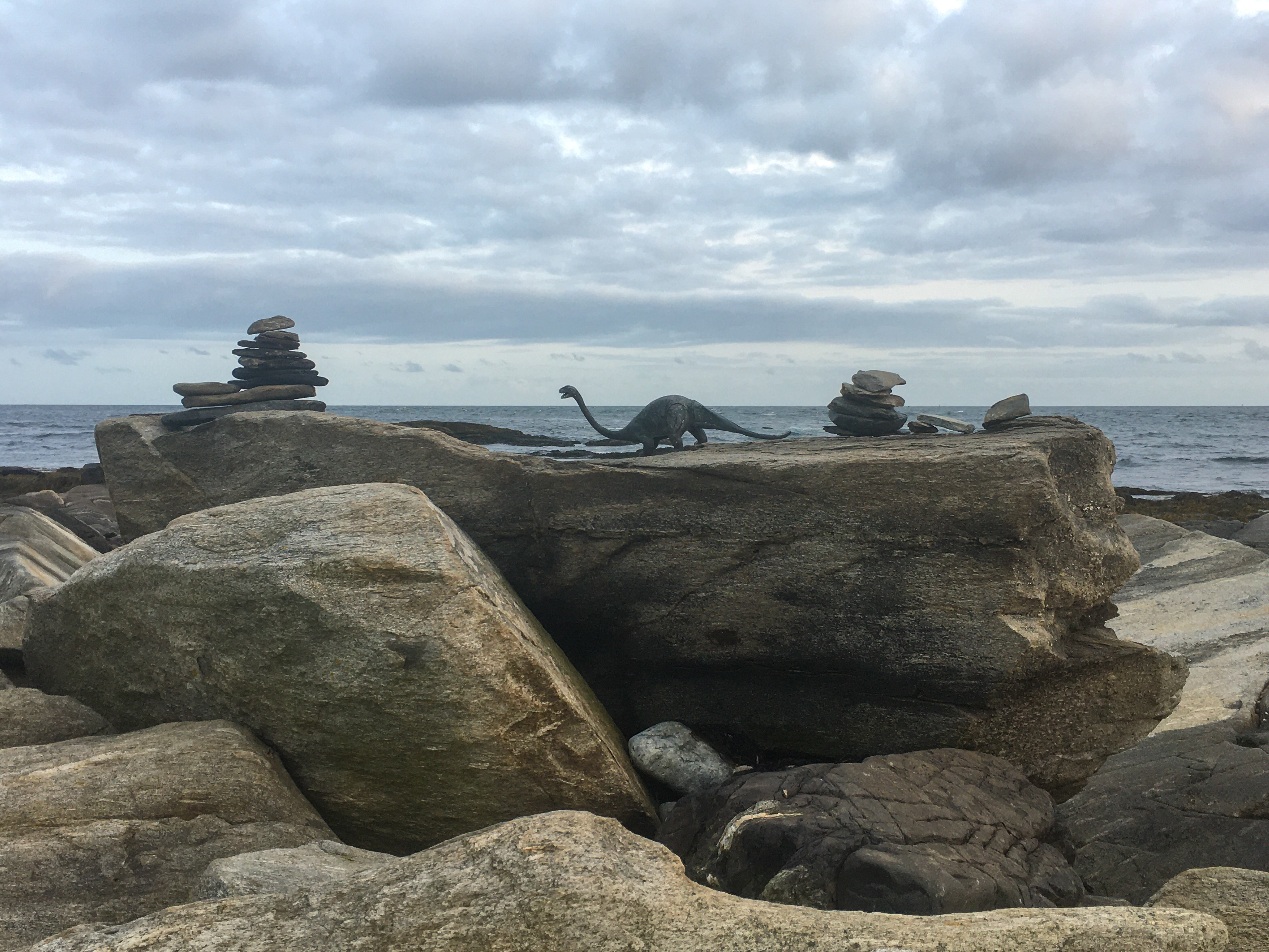 a plastic dinosaur on a rock overlooking the ocean