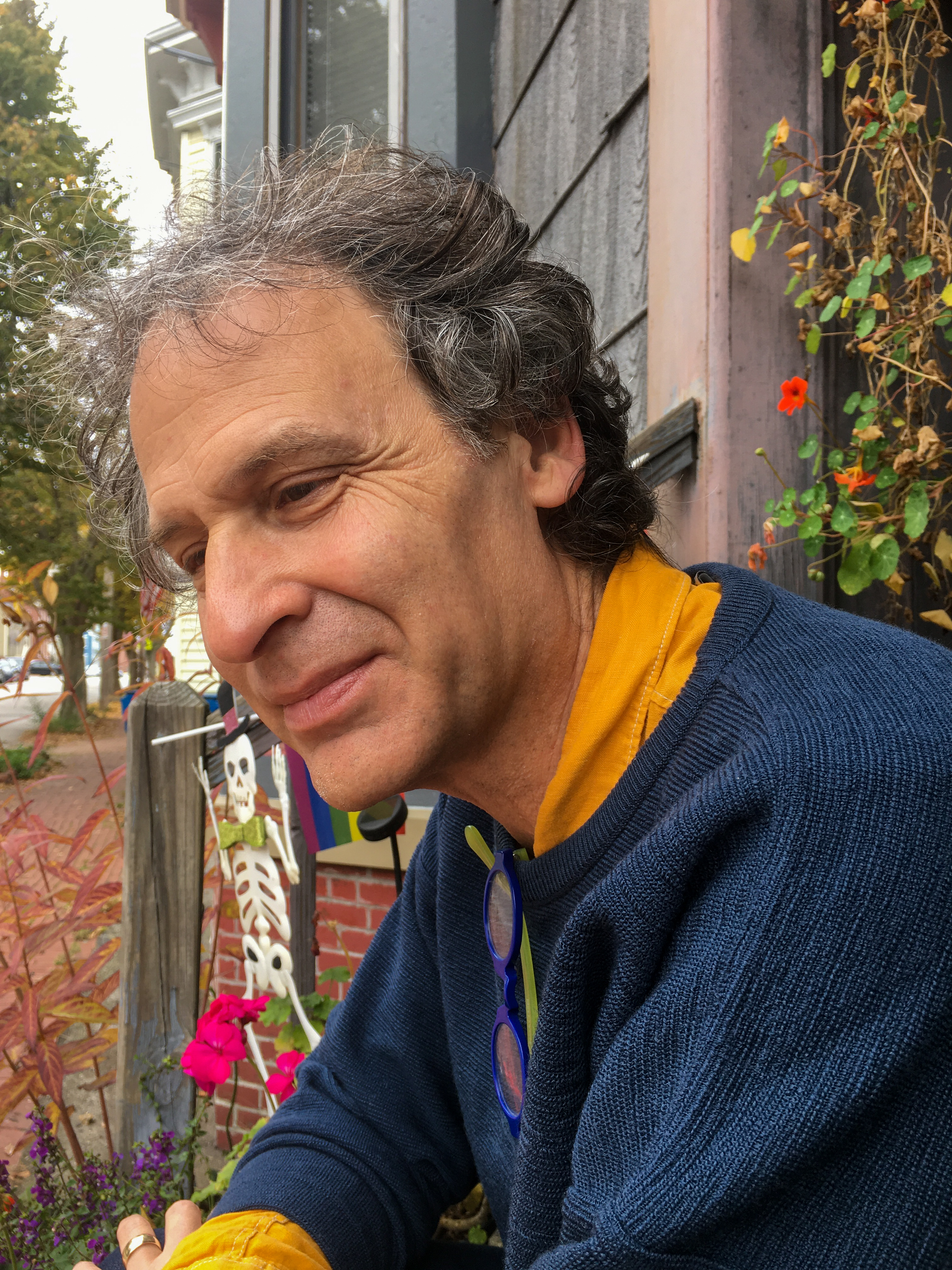 Man sitting smiling in a blue sweater and yellow shirt surrounded by flowers