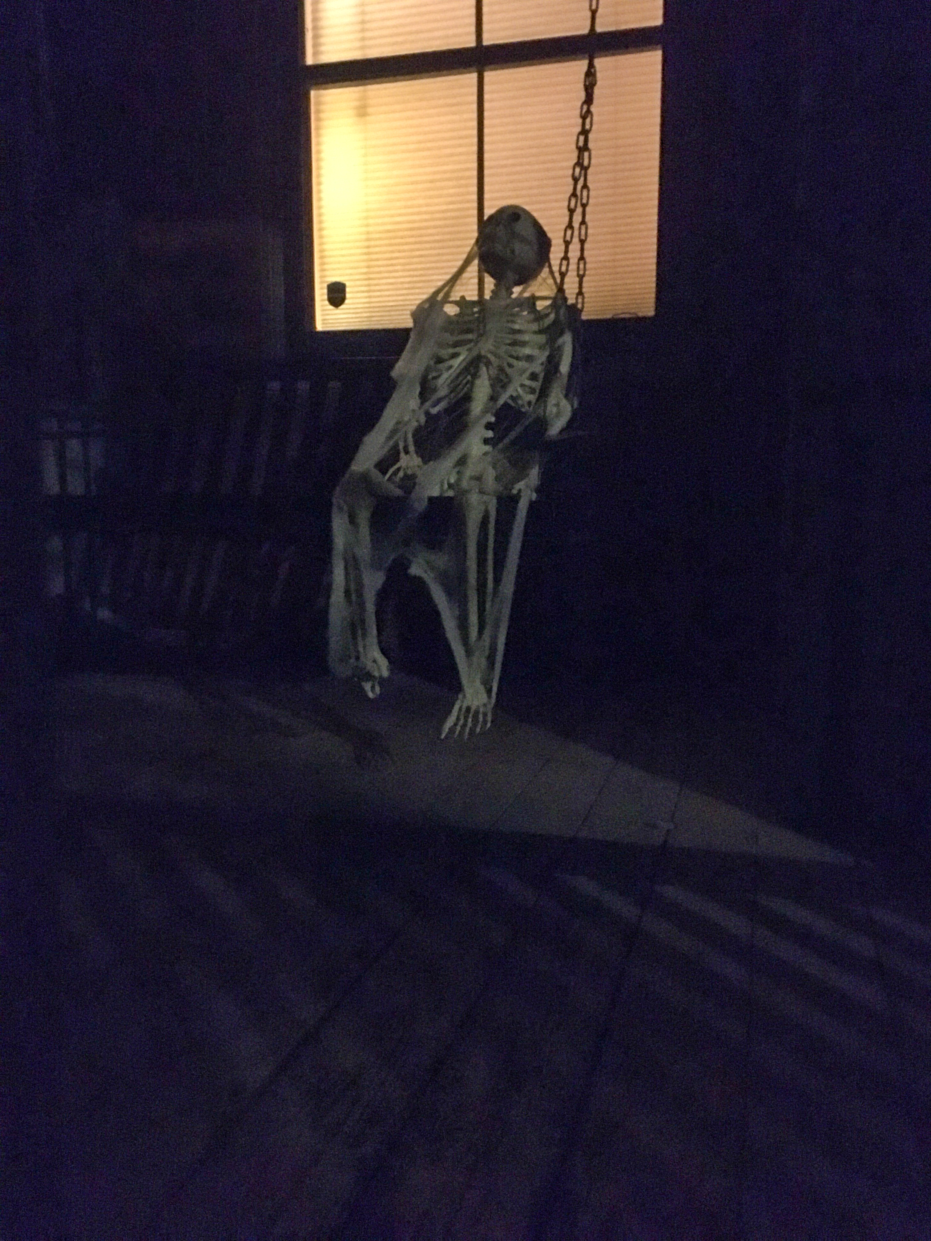 skeleton sitting in a bench rocking swing on a porch covered with cobwebs for halloween 