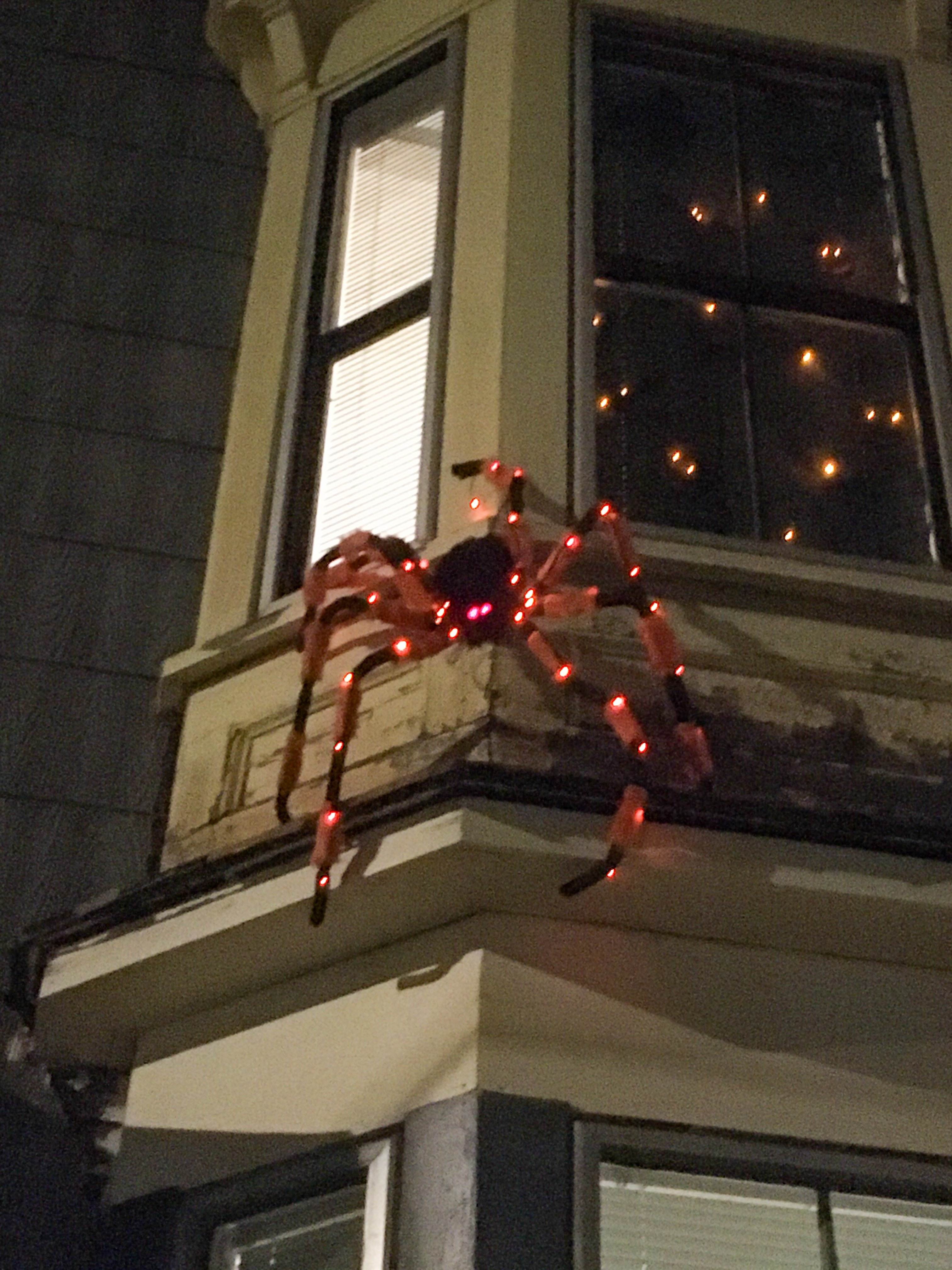 spider lit up with orange light on the outside of a house