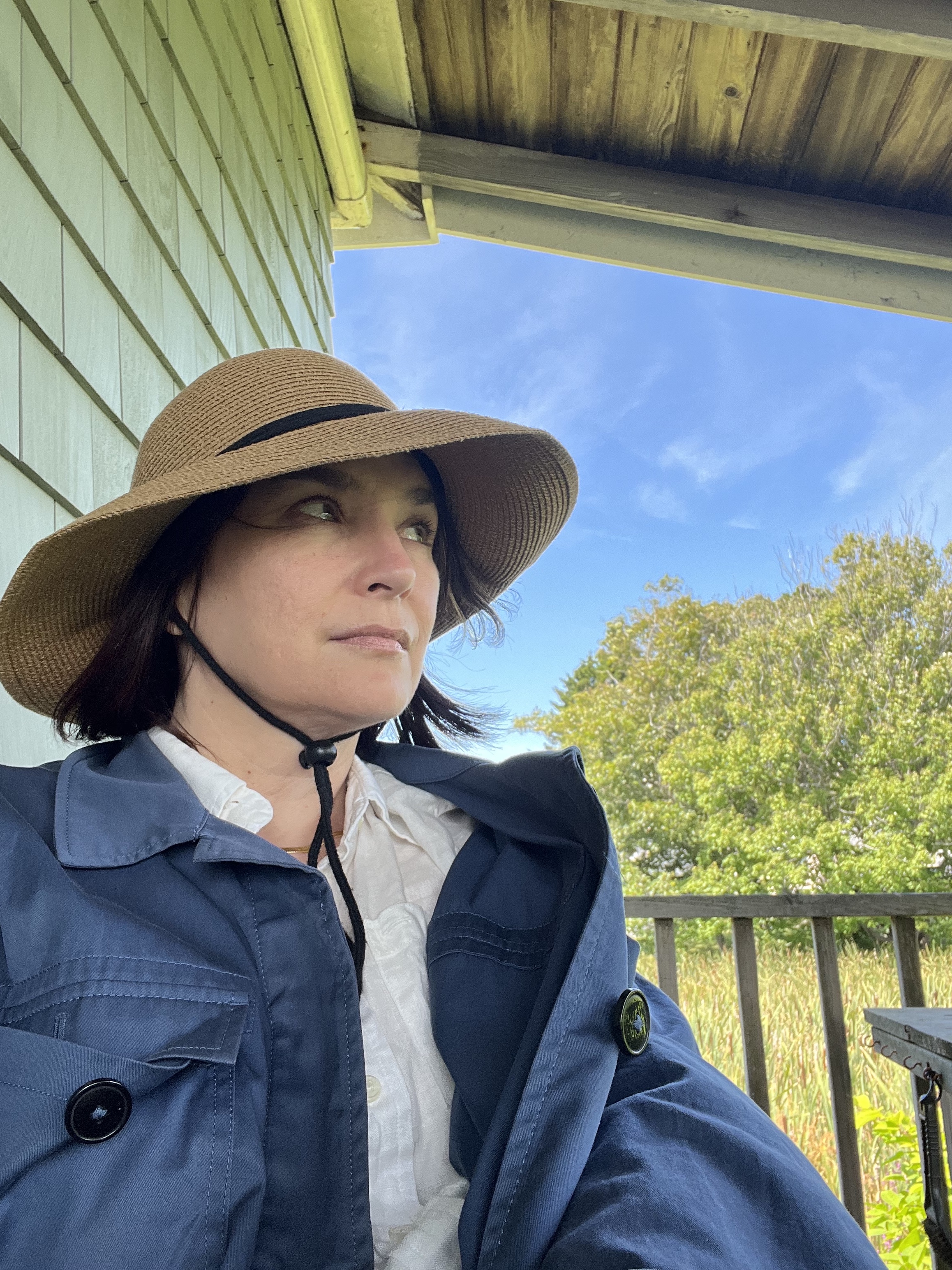 woman sitting on a porch in a sun hat wearing a blue jacket